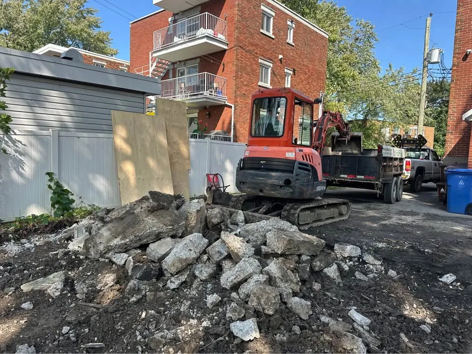 Pile of broken concrete slabs in a lane, with a compact excavator and trailer behind