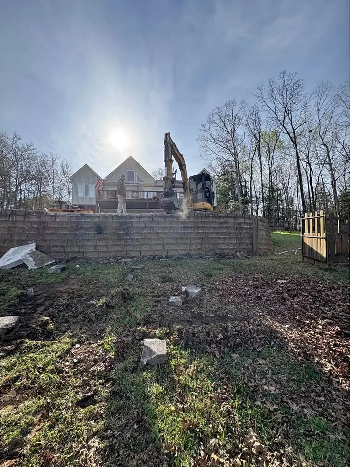 Excavator working behind a block retaining wall on a backyard slope