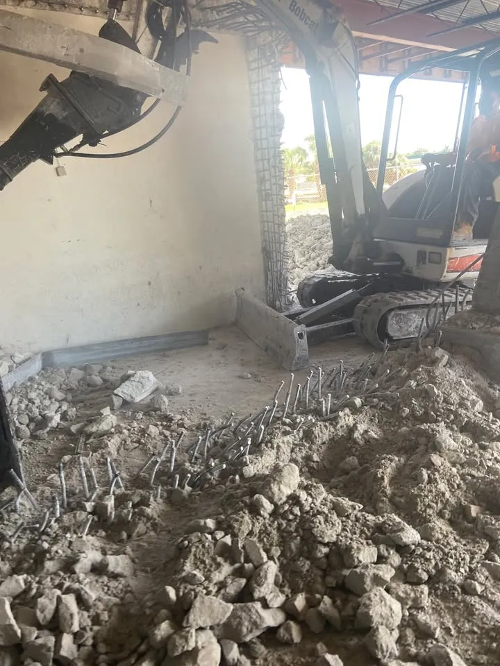 Mini excavator breaking out a concrete floor slab inside a building, rebar exposed