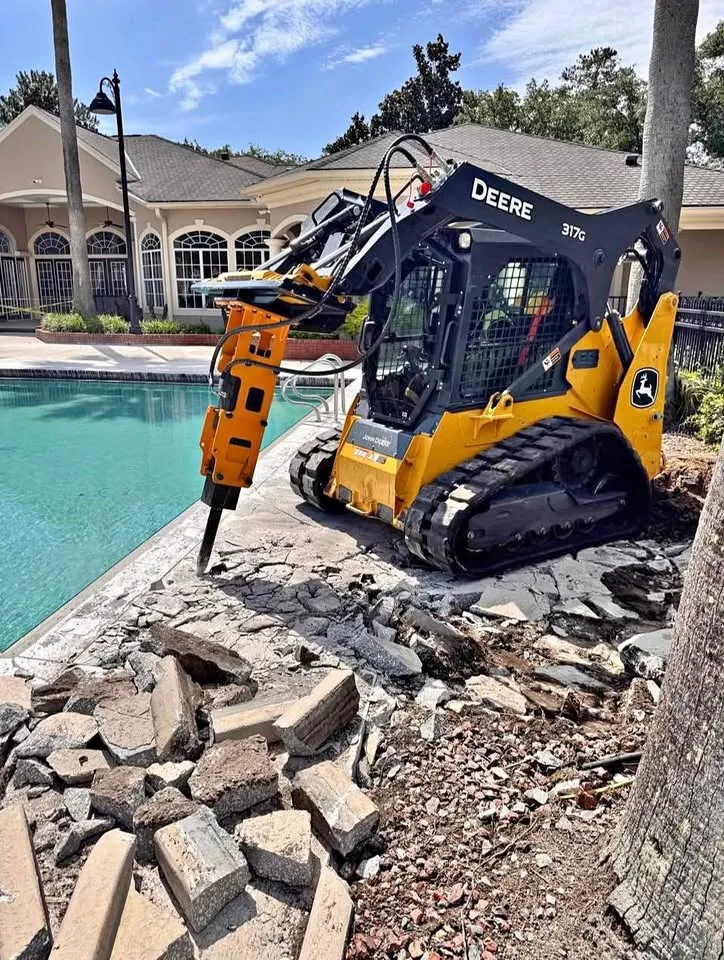 Compact track loader with a hydraulic breaker splitting a concrete pool deck