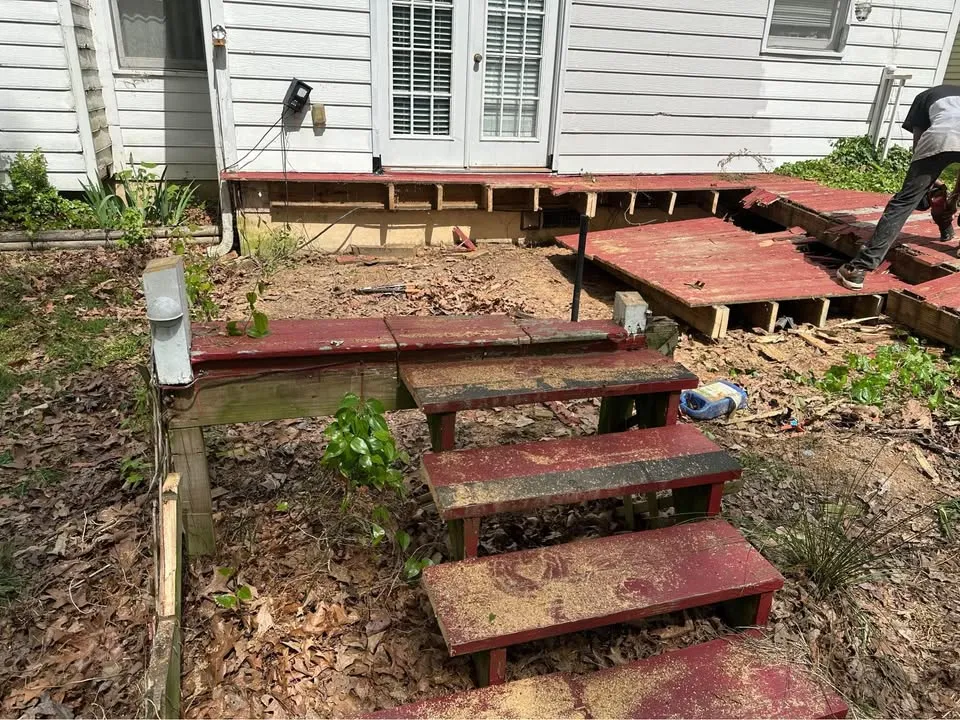 Red backyard deck and stairs partly dismantled beside a house