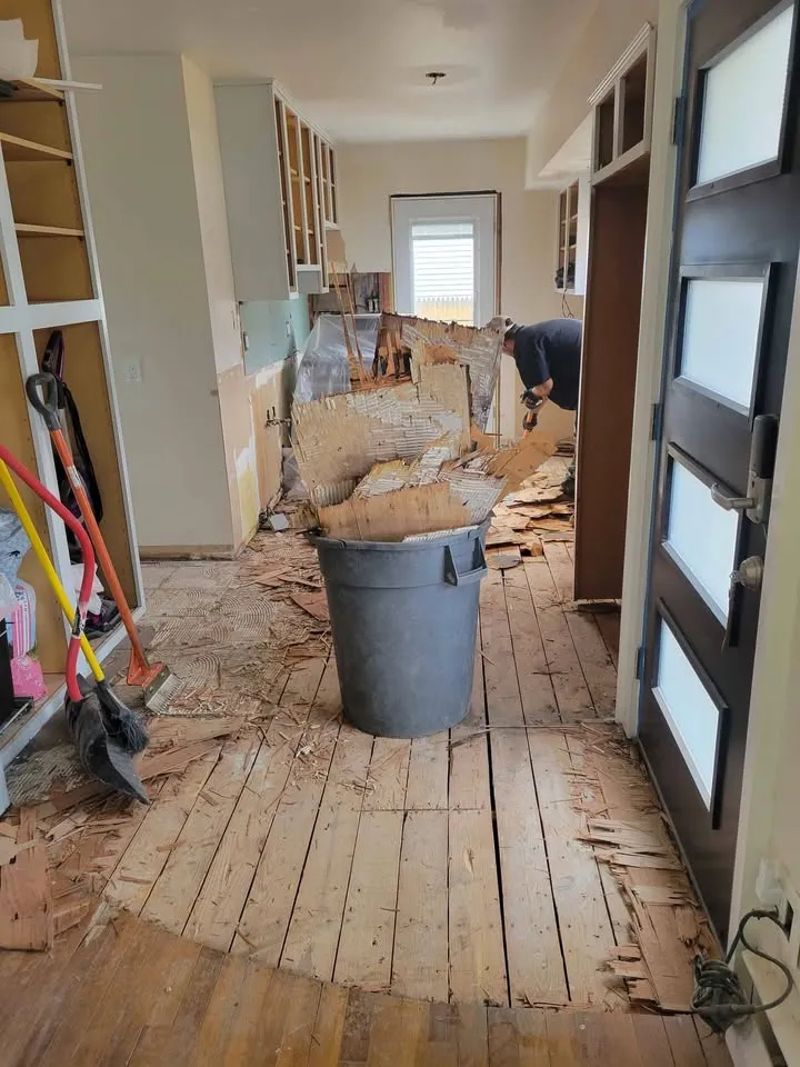 Kitchen floor torn up to the planks with a debris bin in the middle of the room