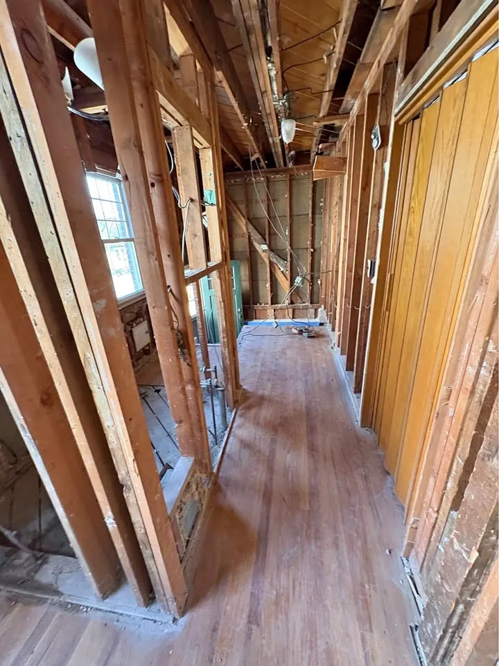 Hallway stripped to the studs with the ceiling open and hardwood floor left in place