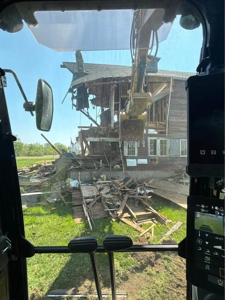 View from inside an excavator cab as the bucket pulls apart a two-storey house