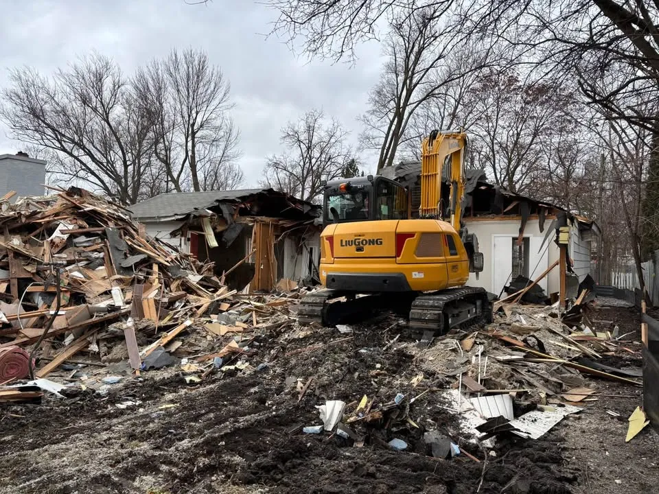 Compact excavator standing in the rubble of a house that is half taken down