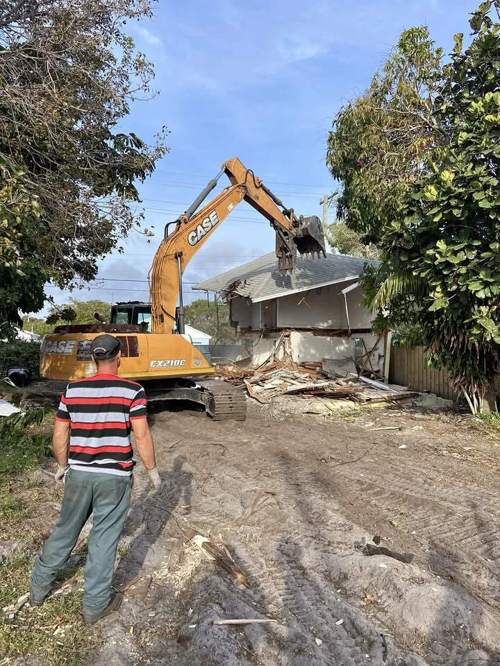 Crew member watching an excavator work across a cleared residential lot