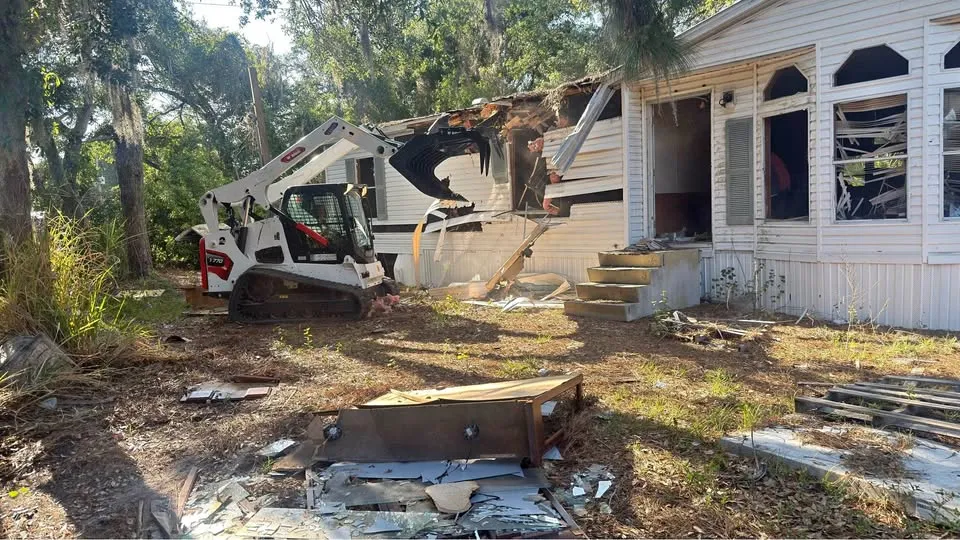 Compact track loader removing debris from the front of a partly demolished house