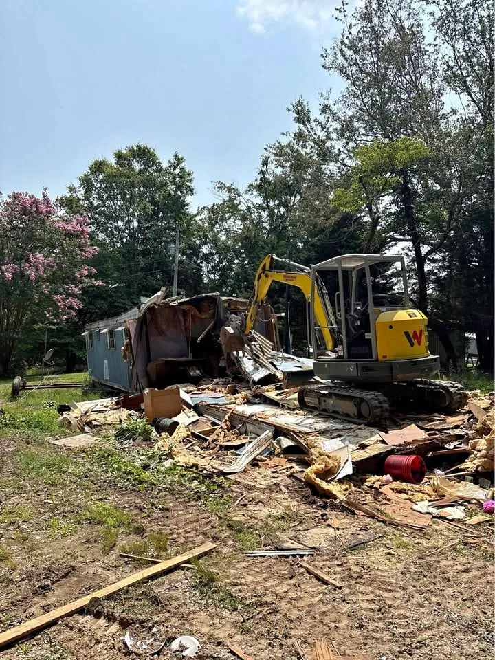 Mini excavator breaking down a small outbuilding in an overgrown yard