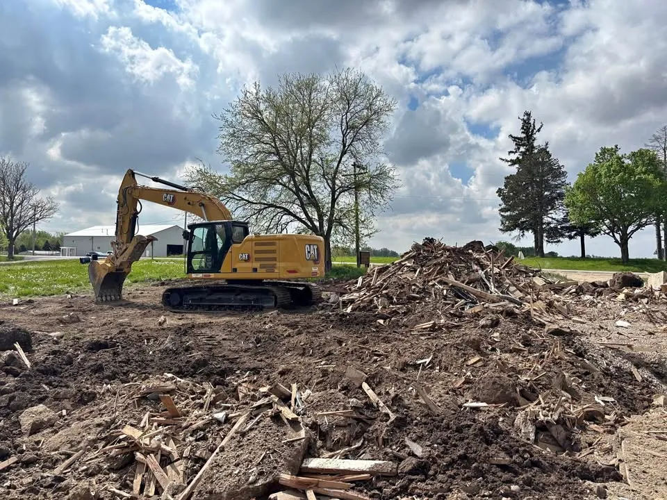 Excavator parked next to a large pile of mixed timber debris on a cleared country lot
