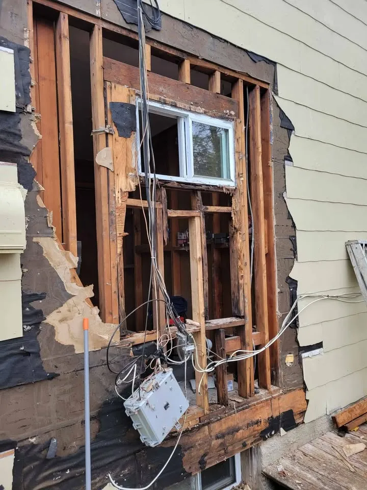 Exterior wall opened to the studs around a window, with siding cut back cleanly