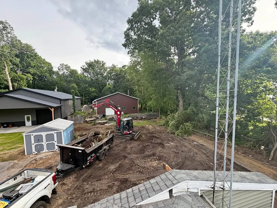 Aerial view of a mini excavator and dump trailer clearing a narrow backyard