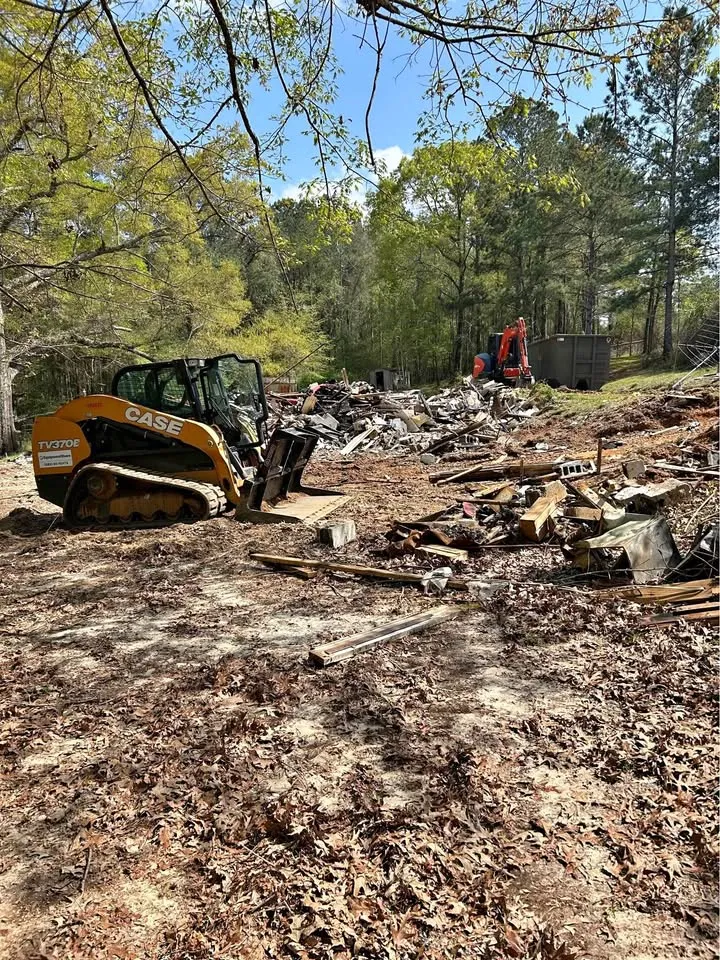 Compact track loader pushing timber debris across a wooded lot