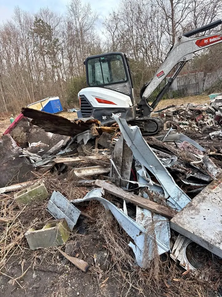 Mini excavator sorting twisted metal and wood debris on a cleared site