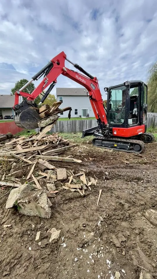 Red mini excavator working on a pile of broken wood and masonry