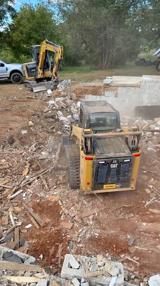 Compact track loader and excavator clearing masonry rubble from a lot